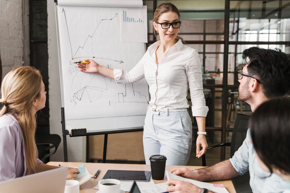 A confident executive assistant presenting a successful project strategy on a screen to an approving CEO in a modern office, illustrating the "great" dynamic of proactive partnership.
